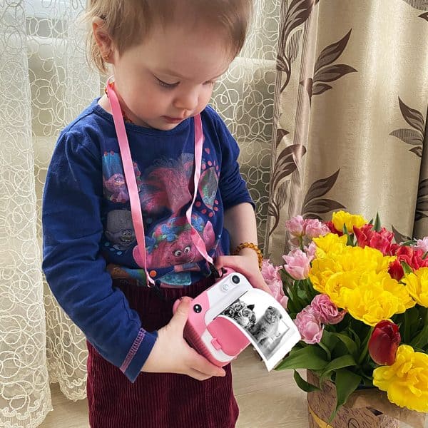 ילדה קטנה מחזיקה מצלמה מדפיסה תמונות צבעוניות.